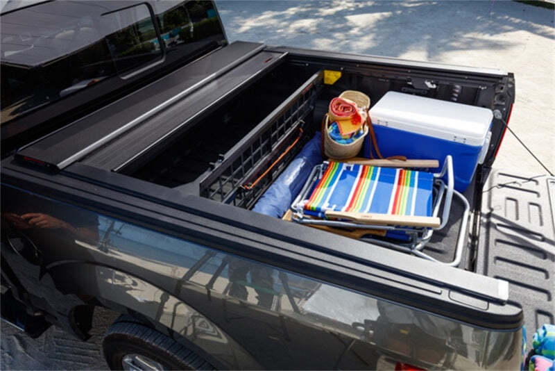 Pickup truck with a Roll-N-Lock retractable bed cover partially open, revealing organized storage of beach gear, cooler, and folding chairs, ideal for keeping items secure and easily accessible.